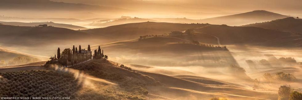 Schöne Toskana Landschaft mit Wiesen Hügeln und Feldern mit lichtdurchflutetem Nebel bei einem stahlenden Sonnenaufgang.